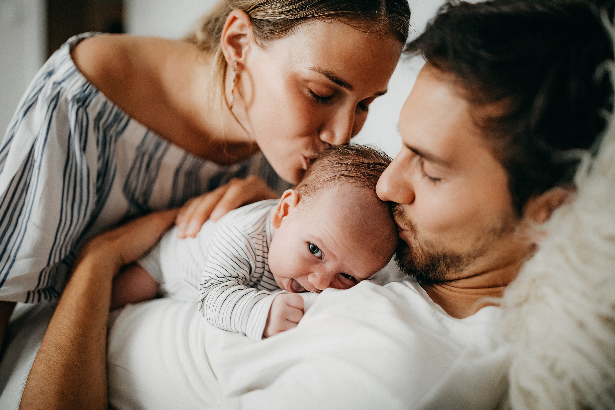 Family laying down in bed with baby in arms